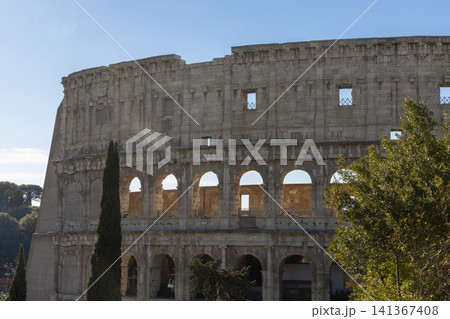 Famous Coliseum in Rome. Colosseum, or Coliseum. Part of the wall of an antique stone structure with arches. Italy, Europe. Famous touristic place in the world, Europe. Beautiful blue sky background. Famous Coliseum in Rome. Colosseum, or Coliseum. Part of the wall of an antique stone structure with arches. Italy, Europe. Famous touristic place in the world, Europe. Beautiful blue sky background. 141367408