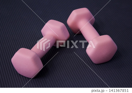 It is a pink dumbbell placed on a yoga mat. It is a pink dumbbell placed on a yoga mat. 141367851