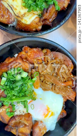 Japanese barbecue chicken rice bowl with soft poached egg, scallions, glazed grilled meat, and noodles served in black bowls on wooden table, warm rich comfort food closeup Japanese barbecue chicken rice bowl with soft poached egg, scallions, glazed grilled meat, and noodles served in black bowls on wooden table, warm rich comfort food closeup 141367903
