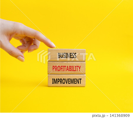 Business profitability improvement symbol. Concept word Business profitability improvement on wooden blocks. Beautiful yellow background. Businessman hand. Business and Business profitability Business profitability improvement symbol. Concept word Business profitability improvement on wooden blocks. Beautiful yellow background. Businessman hand. Business and Business profitability 141368909
