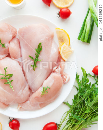 Fresh raw chicken breast meat on plate with greens fresh vegetables and fruits preparing for cooking Fresh raw chicken breast meat on plate with greens fresh vegetables and fruits preparing for cooking 141369210