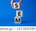 SEM - Search Engine Marketing symbol. Wooden cubes with words SEM. Businessman hand. Beautiful blue background. Business and SEM concept. Copy space. 141369390