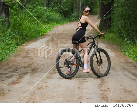 Woman cyclist riding bicycle on forest road. Girl spending active time in nature during summer. Sporty lifestyle, fitness training and outdoor recreation activity in green park. Woman cyclist riding bicycle on forest road. Girl spending active time in nature during summer. Sporty lifestyle, fitness training and outdoor recreation activity in green park. 141369767