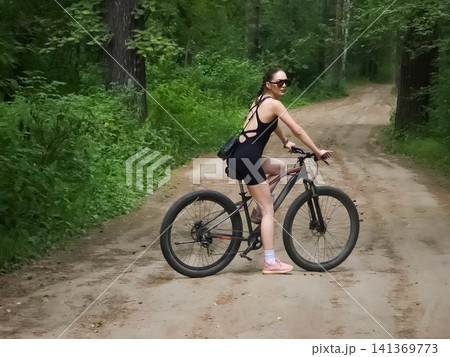 Woman cyclist riding a mountain bike on a forest path. Young girl enjoying a outdoor bicycle ride in nature. Healthy lifestyle activity, active recreation and fitness training concept. 141369773