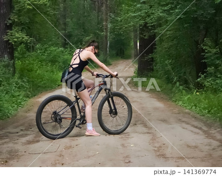 Woman cyclist resting on forest path. Girl riding mountain bicycle in nature. Sports active lifestyle, outdoor adventure, summer travel, training, fitness and healthy exercise concept. Woman cyclist resting on forest path. Girl riding mountain bicycle in nature. Sports active lifestyle, outdoor adventure, summer travel, training, fitness and healthy exercise concept. 141369774