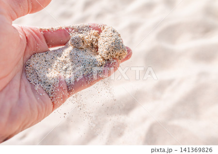 砂浜で手のひらからこぼれ落ちる白い砂 砂浜で手のひらからこぼれ落ちる白い砂 141369826
