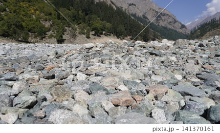 Rocky riverbed in the foreground with a steep mountain face and blue sky in background, alpinescape concept. Rocky riverbed in the foreground with a steep mountain face and blue sky in background, alpinescape concept. 141370161