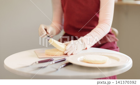 Hands in gloves using cake leveler to slice sponge layer on white table for baking preparation 141370392