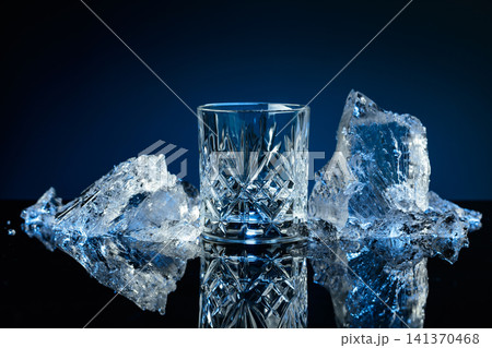 Crystal glass of vodka and ice shards against a black reflective background. Crystal glass of vodka and ice shards against a black reflective background. 141370468