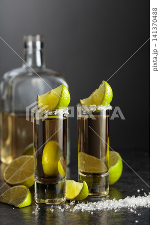 Tequila shots with salt and lime slices on a black stone table. Tequila shots with salt and lime slices on a black stone table. 141370488