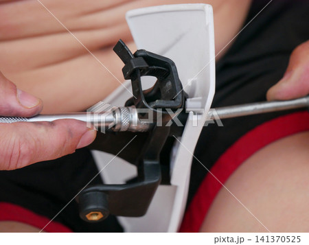 Man using screwdriver or socket wrench to assemble plastic component. Mechanic repairing mechanical part or performing home improvement task. Close up of hands fixing equipment. 141370525