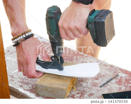 Man using electric drill to make hole in white plastic part on wooden piece. Manual worker repairing equipment. Construction, diy project and handyman home improvement concept. 141370530