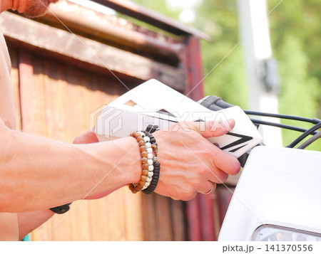 Man inspecting motorcycle handlebar with hand guards. Mechanic repairing dirt bike detail. Close up shot of hands with beaded bracelets touching vehicle component. Outdoor maintenance concept. Man inspecting motorcycle handlebar with hand guards. Mechanic repairing dirt bike detail. Close up shot of hands with beaded bracelets touching vehicle component. Outdoor maintenance concept. 141370556