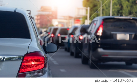 Rear view shot of several cars traveling in heavy traffic on an urban highway. Bright red tail light of the closest car is prominently displayed during the sunny daytime commute. City of Thailand. 141370575