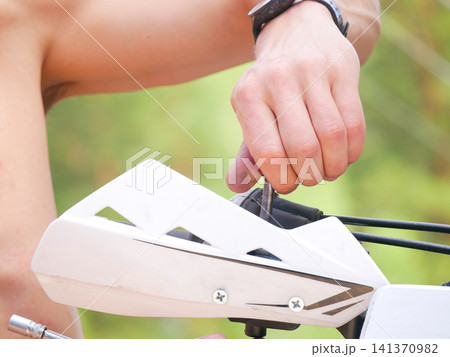 Man mechanic repairing motorcycle handlebar. Motorcyclist using tool to fix bike component. Maintenance and service of offroad vehicle. Engineering and technical mechanical work concept. Man mechanic repairing motorcycle handlebar. Motorcyclist using tool to fix bike component. Maintenance and service of offroad vehicle. Engineering and technical mechanical work concept. 141370982