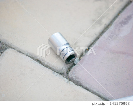 Metal socket head for ratcheting wrench lying on stone tile floor. Industrial tool component for mechanical repair, maintenance or hardware workshop. Professional equipment hardware. Metal socket head for ratcheting wrench lying on stone tile floor. Industrial tool component for mechanical repair, maintenance or hardware workshop. Professional equipment hardware. 141370998