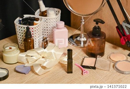 Makeup and skincare items arranged on a wooden table in a simple room during daytime 141371022