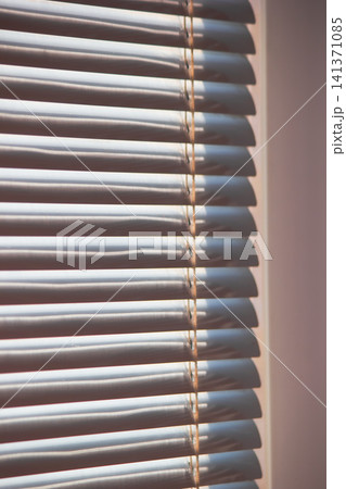 Close up of modern white window blinds filtering bright daylight Close up of modern white window blinds filtering bright daylight 141371085