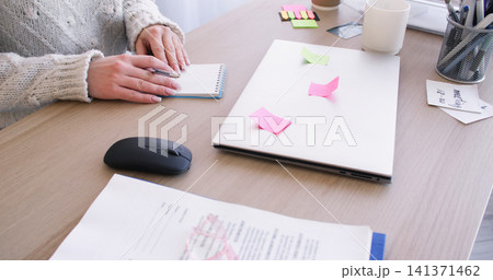 Office workflow. Freelance lifestyle. Unrecognizable female entrepreneur working at desk writing task with sticky notes on laptop indoor. Office workflow. Freelance lifestyle. Unrecognizable female entrepreneur working at desk writing task with sticky notes on laptop indoor. 141371462