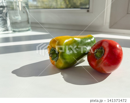 Fresh bell peppers on white kitchen countertop in natural sunlight with clean minimal home interior. Healthy nutrition, cooking, vegetarian lifestyle, fresh produce, meal preparation, wellness, food Fresh bell peppers on white kitchen countertop in natural sunlight with clean minimal home interior. Healthy nutrition, cooking, vegetarian lifestyle, fresh produce, meal preparation, wellness, food 141371472