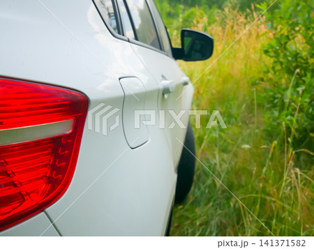 White car parked on grassy roadside. Exterior view of modern vehicle rear light during road trip. Concept of travel, leisure, nature escape, transport adventure, outdoor weekend getaway. White car parked on grassy roadside. Exterior view of modern vehicle rear light during road trip. Concept of travel, leisure, nature escape, transport adventure, outdoor weekend getaway. 141371582