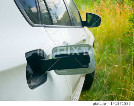 Car with open electric charging port. Hybrid vehicle charging socket on white automobile for energy efficiency. Modern sustainable transportation and eco friendly technology concept. Car with open electric charging port. Hybrid vehicle charging socket on white automobile for energy efficiency. Modern sustainable transportation and eco friendly technology concept. 141371583