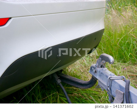 Car towing system with metal hitch and trailer coupling connected to white vehicle bumper. Close up view of vehicle tow bar mechanism for transportation and travel logistics concept. Car towing system with metal hitch and trailer coupling connected to white vehicle bumper. Close up view of vehicle tow bar mechanism for transportation and travel logistics concept. 141371602