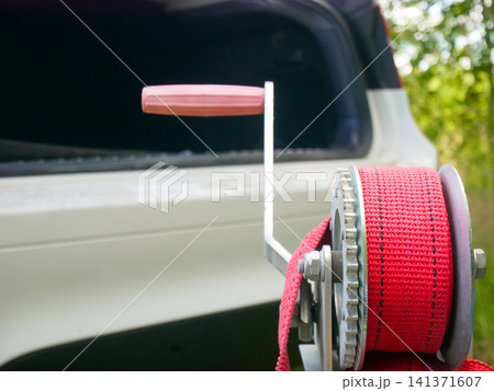 Hand winch with red strap mounted on trailer for boat or vehicle. Mechanical manual pulling tool for securing cargo and towing equipment. Heavy duty hardware for transport logistics. Hand winch with red strap mounted on trailer for boat or vehicle. Mechanical manual pulling tool for securing cargo and towing equipment. Heavy duty hardware for transport logistics. 141371607