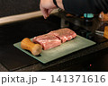 Hand Sprinkling Pepper on Seasoned Raw Pork Steaks Board 141371616
