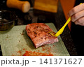 Pouring Dark Sauce From Bottle Over Seasoned Raw Pork Loin 141371627