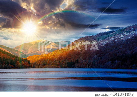 landscape with lake in autumn. day meet night. sun and moon over scenic view of forest reflection on the lake surface at twilight. rika river water reserve. transcarpathia in fall season. astrology landscape with lake in autumn. day meet night. sun and moon over scenic view of forest reflection on the lake surface at twilight. rika river water reserve. transcarpathia in fall season. astrology 141371878