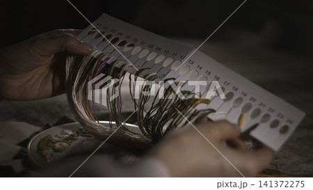 Woman Chooses Thread. Carefully Selecting Thread Shades From Numbered Color Swatches For Embroidery. Media Woman Chooses Thread. Carefully Selecting Thread Shades From Numbered Color Swatches For Embroidery. Media 141372275