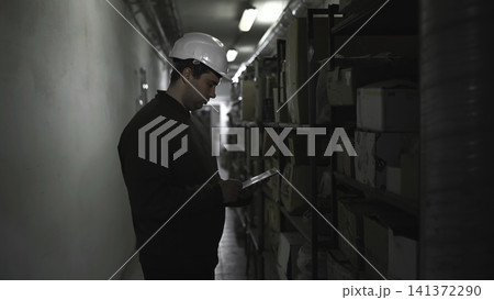 Auditor Checks Inventory. Employee Systematically Inspects Inventory In Restricted Storage Corridor. Media Auditor Checks Inventory. Employee Systematically Inspects Inventory In Restricted Storage Corridor. Media 141372290
