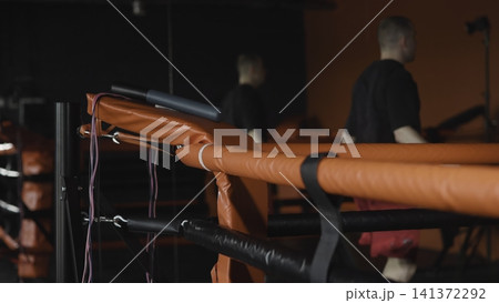Boxing ring corner with bright orange padded ropes, vinyl turnbuckle cover, metal post hardware, and blurred figures moving near edge during training session, with boxing, ring, corner, rope detail Boxing ring corner with bright orange padded ropes, vinyl turnbuckle cover, metal post hardware, and blurred figures moving near edge during training session, with boxing, ring, corner, rope detail 141372292