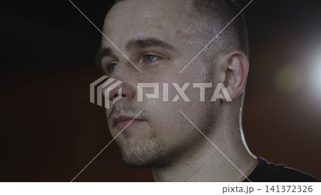 Sweaty young male portrait in warm rim light, tight three-quarter profile with shallow interior focus, showing post-workout intensity, skin texture, stubble, and calm expression Sweaty young male portrait in warm rim light, tight three-quarter profile with shallow interior focus, showing post-workout intensity, skin texture, stubble, and calm expression 141372326