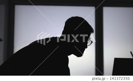 Contemplative Man By Window. Leaning Figure Of Man Lost In Thought At His Laptop Near Lit Window. Media 141372350
