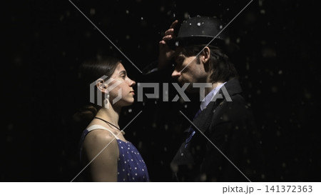 Man tipping his hat toward a woman in falling snow Man tipping his hat toward a woman in falling snow 141372363