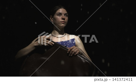Young woman playing a string instrument on a dark stage Young woman playing a string instrument on a dark stage 141372411