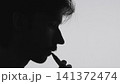 Relaxed side profile silhouette of man smoking cigarette against neutral background with clean natural light, strong contrast, minimal composition, commercial concept, calm atmosphere 141372474