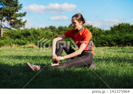 Woman stretches on grass in sunny outdoor location Woman stretches on grass in sunny outdoor location 141373904