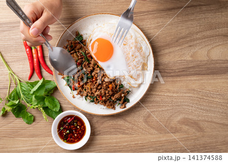 Eating Thai food, Stir-fried holy basil with minced pork with cooked rice and fried egg Eating Thai food, Stir-fried holy basil with minced pork with cooked rice and fried egg 141374588