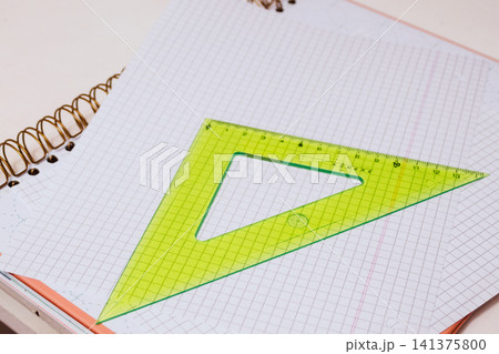 Green set square lying on a grid paper notebook, symbolizing geometry, mathematics, and education, representing school, learning, and study concepts for students and colleges Green set square lying on a grid paper notebook, symbolizing geometry, mathematics, and education, representing school, learning, and study concepts for students and colleges 141375800