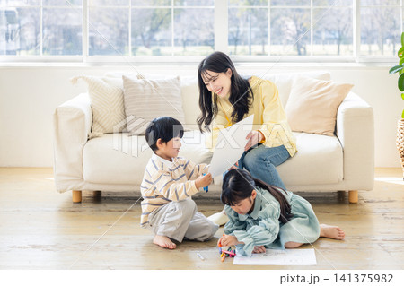 ソファに座り子供たちが描いた絵を笑顔で褒める母親 ソファに座り子供たちが描いた絵を笑顔で褒める母親 141375982
