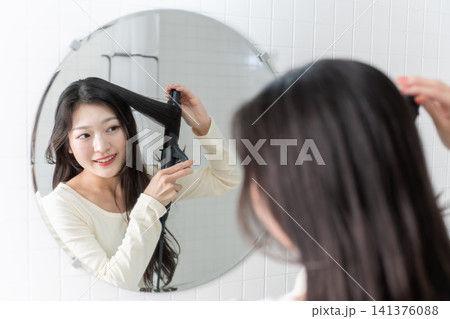 洗面台でヘアアイロンを使って髪を巻く若い女性 ビューティーイメージ 洗面台でヘアアイロンを使って髪を巻く若い女性 ビューティーイメージ 141376088