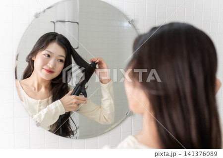洗面台でヘアアイロンを使って髪を巻く若い女性 ビューティーイメージ 141376089