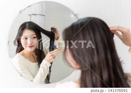 洗面台でヘアアイロンを使って髪を巻く若い女性 ビューティーイメージ 洗面台でヘアアイロンを使って髪を巻く若い女性 ビューティーイメージ 141376091