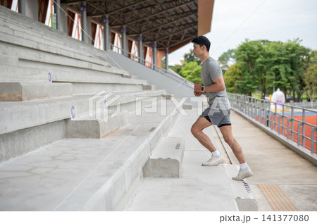 Fit Asian athletic man running up the concrete seating stairs before exercise in sports stadium. 141377080
