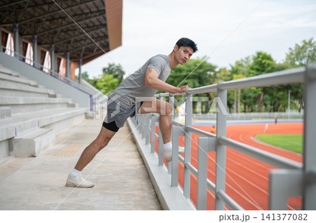 Athletic Asian man stretching leg muscles on a railing before exercise in sports stadium. 141377082