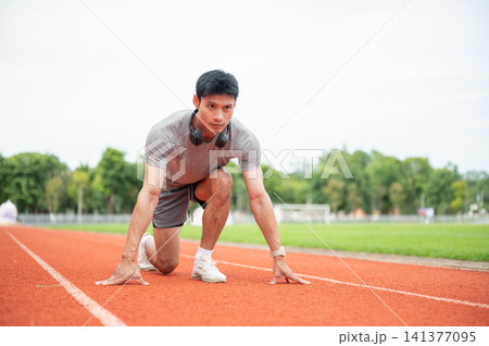 Asian man sprinter focused while crouching in start position ready to run on track in sports stadium 141377095