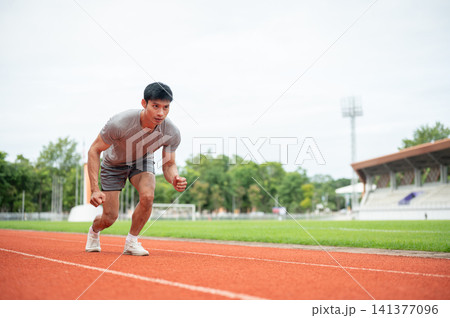 Asian athletic man launching from start line on running track in sports stadium. Asian athletic man launching from start line on running track in sports stadium. 141377096